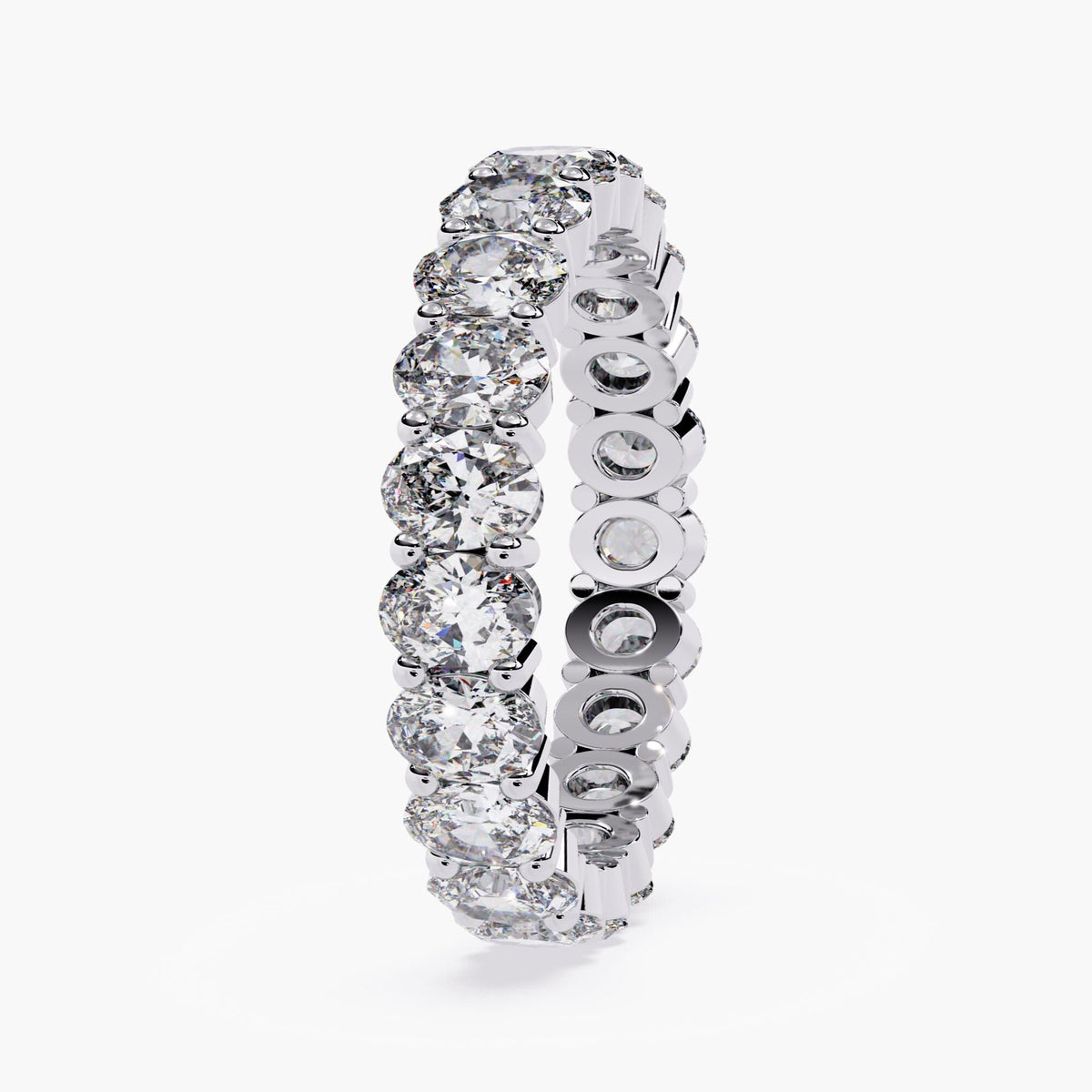 A white gold band ring with a row of oval shaped diamonds set in a pave setting.