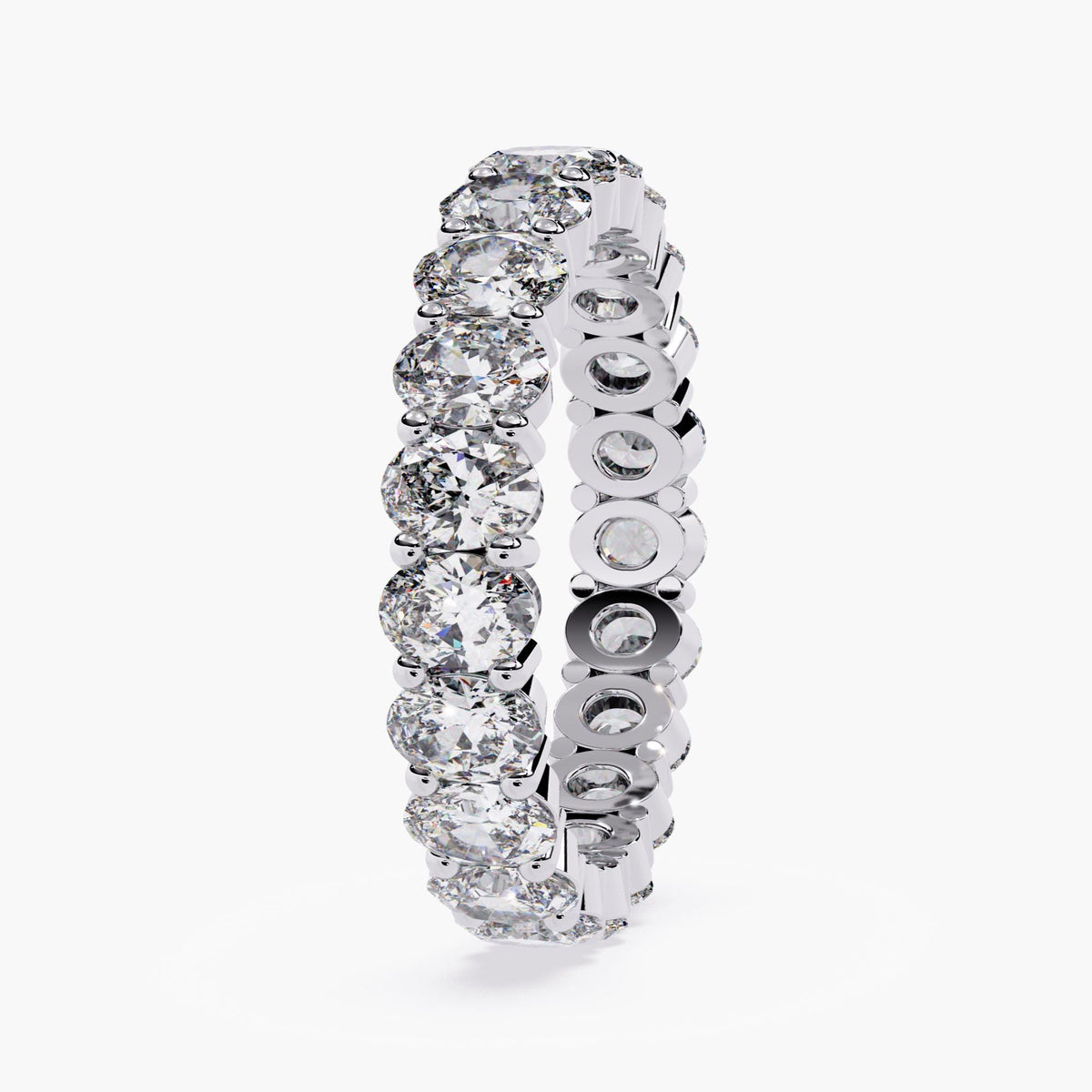 A white gold band ring with a row of oval shaped diamonds set in a pave setting.