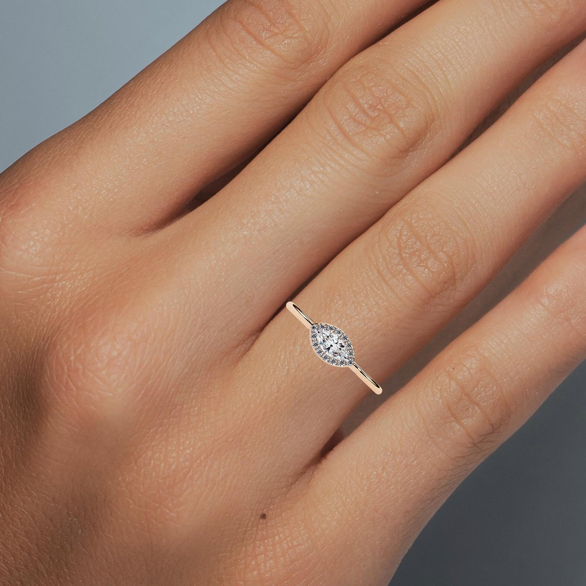 A marquise diamond halo ring in 14k yellow gold, worn on a hand to show scale. The east-west marquise center stone is surrounded by a fine pavé of round diamonds in a halo setting, creating a soft eye-shaped silhouette. Set on a slim polished gold band, the ring has a minimalist yet classic look, ideal as a promise ring, dainty engagement ring, or everyday bridal jewelry.