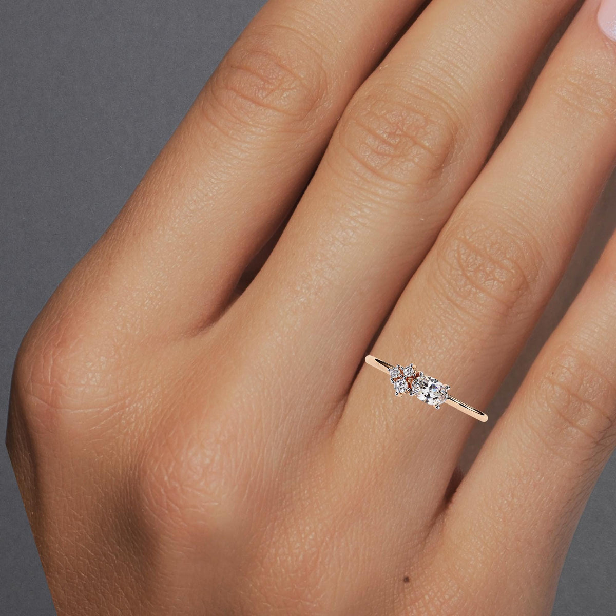 Close-up of a hand wearing a rose gold ring with an east-west oval diamond and a floral cluster of round diamonds, showing the delicate design and slim band in natural lighting.
