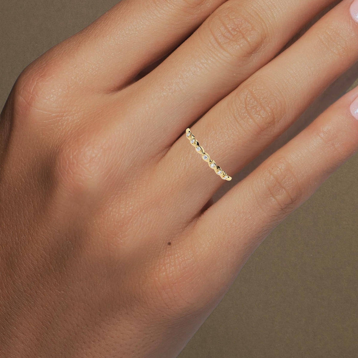 Model wearing a 14k yellow gold seven-stone diamond ring on the ring finger. The dainty band features small round natural diamonds set in alternating pear-shaped bezels, creating a subtle yet unique stacking look perfect for everyday wear.