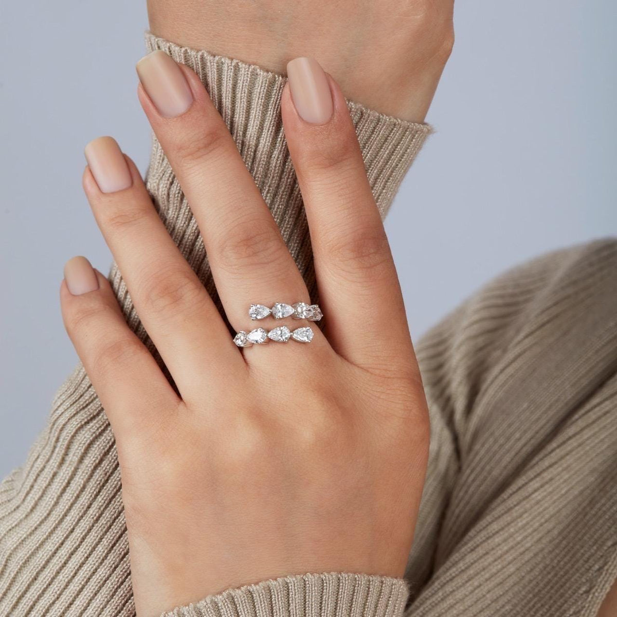 A woman's hand wearing a white gold wrap ring set with pear cut lab grown diamonds. The open bypass design curves around the finger, creating a modern stacked look.