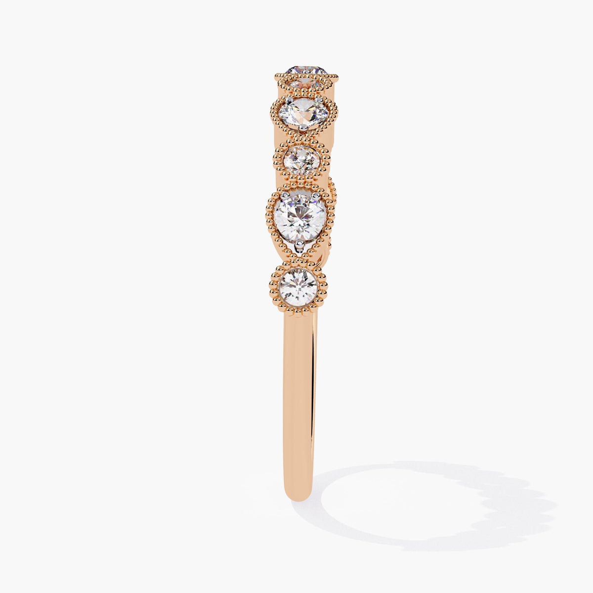 A rose gold band with bezel-set diamonds, each encircled by delicate milgrain detailing. The diamonds, alternating between round and pear-shaped.