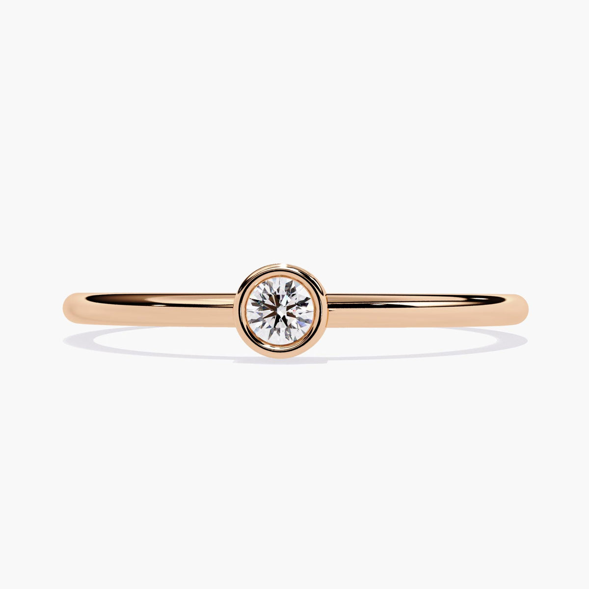 14k rose gold bezel set solitaire ring featuring a single round natural diamond in the center. The diamond is secured in a smooth bezel setting on a thin, polished gold band.