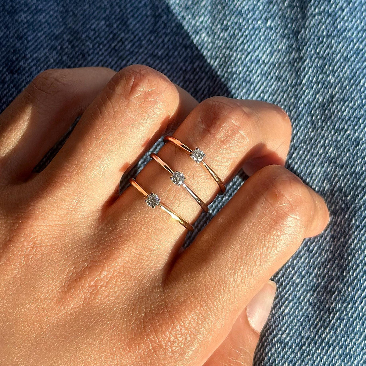 Hand wearing three dainty solitaire rings in 18K rose gold, yellow gold, and white gold, each set with a round lab-grown diamond. Shown in natural light perfect for stacking or minimalist everyday wear.
