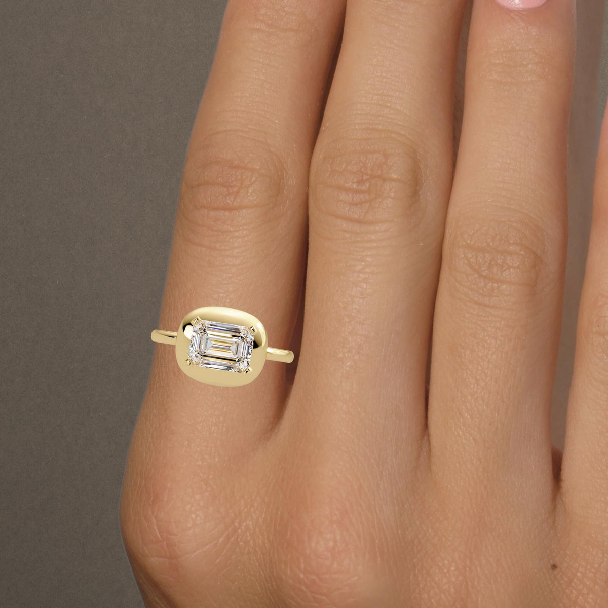 a model wearin East-west emerald cut diamond bezel ring in 14K yellow gold with 1.60 carat IGI-certified lab diamond and a 2mm shank, bold dome design for modern engagement or statement wear. A meaningful gift for birthdays, anniversaries, or celebrating personal milestones.
