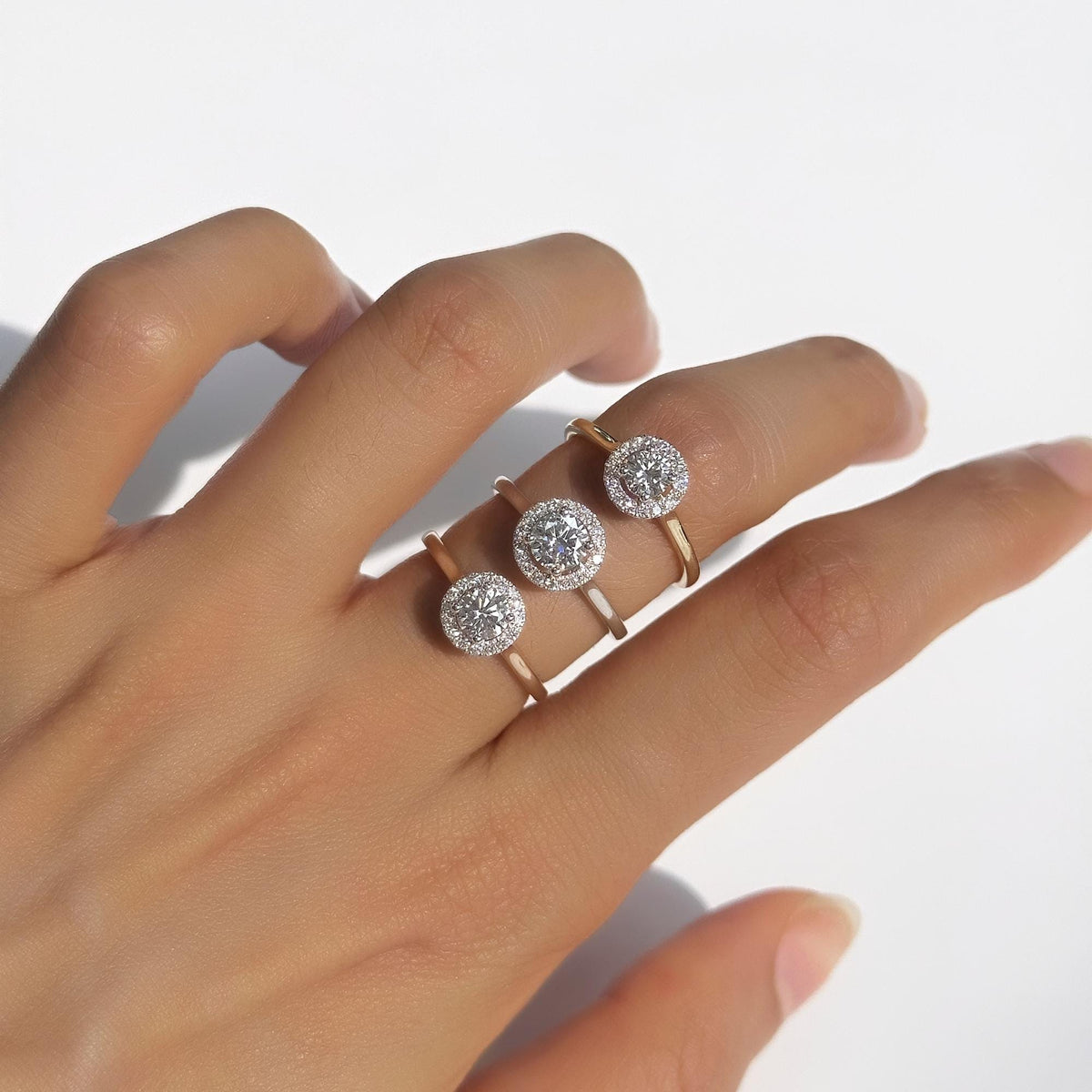 Trio of 18K Gold Halo Diamond Rings worn on hand, featuring round lab-grown center diamonds in 0.30ct, 0.40ct, and 0.50ct sizes. Each ring is set with a pavé diamond halo and a slim, polished straight shank in yellow, white, and rose gold. Minimalist and elegant fine jewelry for everyday wear, engagement, or gifting.