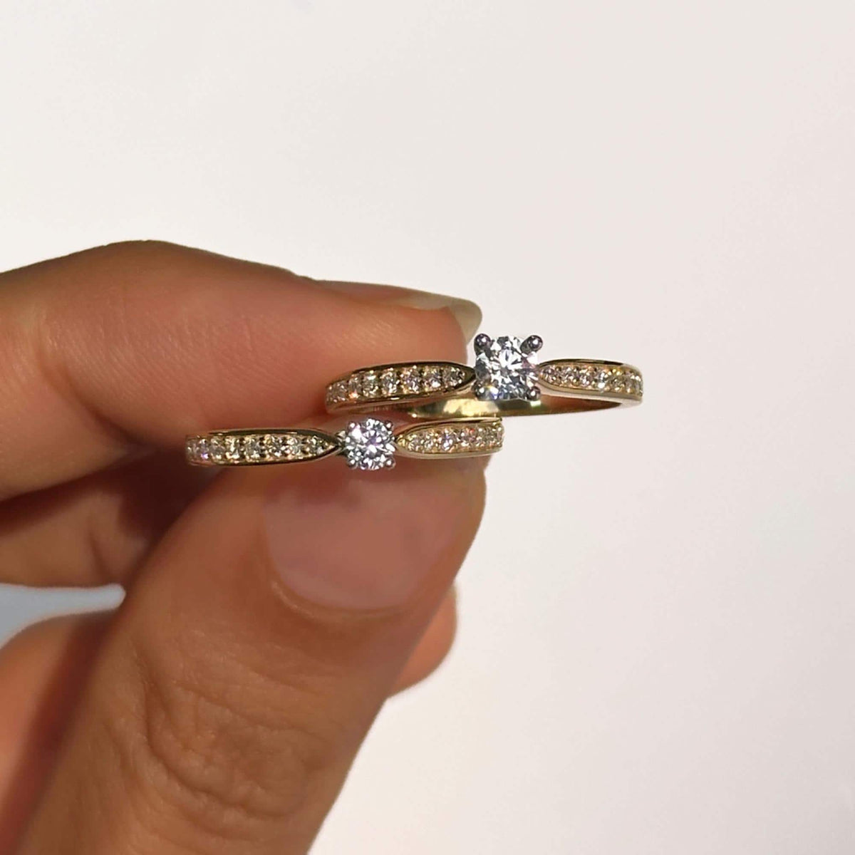 Close-up of two 18K gold half eternity solitaire rings with round lab-grown diamonds held between fingers, showing the difference in center stone sizes and the channel-set pavé detailing.