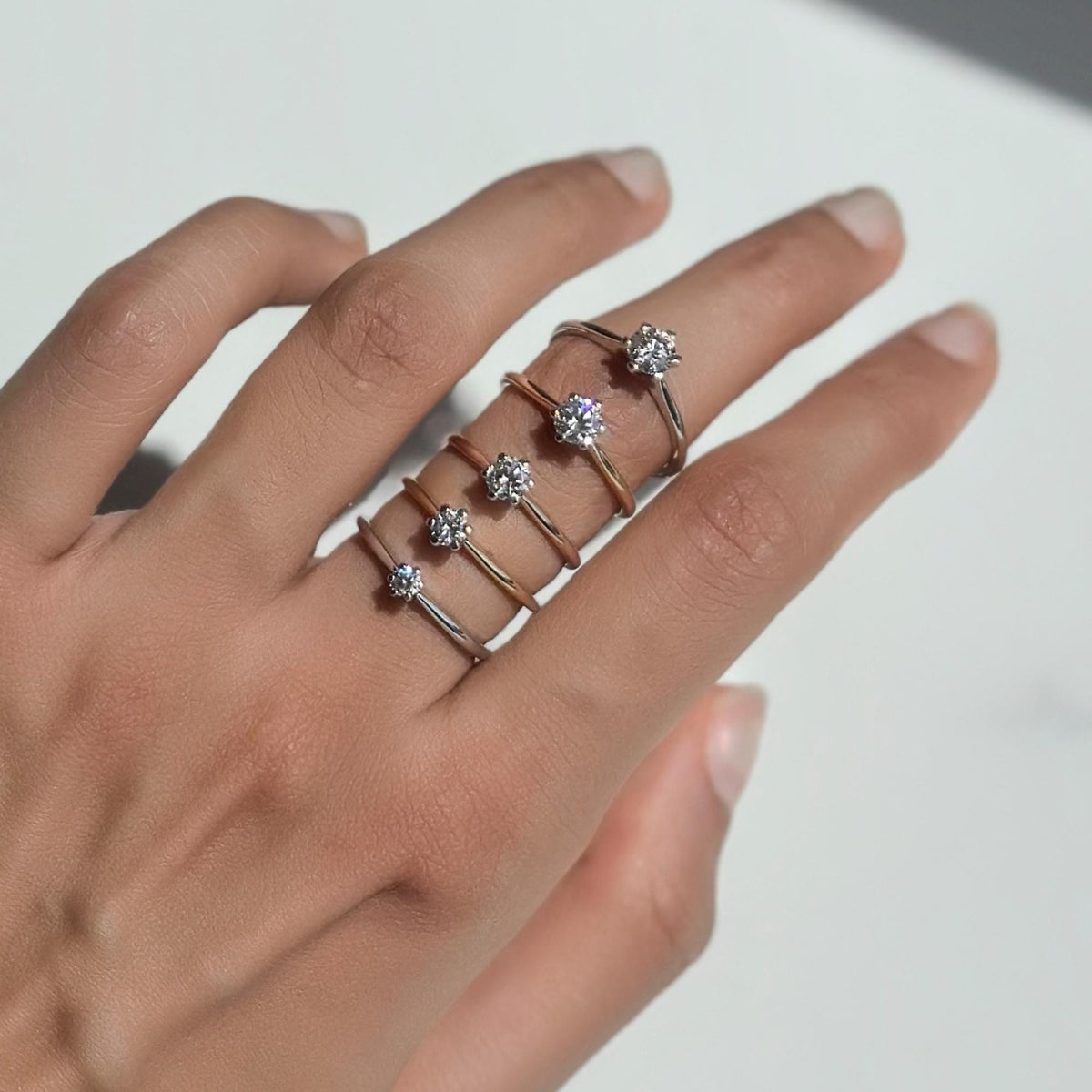Hand wearing a gradient stack of six 18K solid gold solitaire rings, each set with a round cut lab-grown diamond ranging from 0.10 to 0.50 carats in a classic six-prong setting; minimalist and elegant promise or engagement rings available in yellow, rose, and white gold, perfect for everyday wear, proposals, or meaningful gifting.