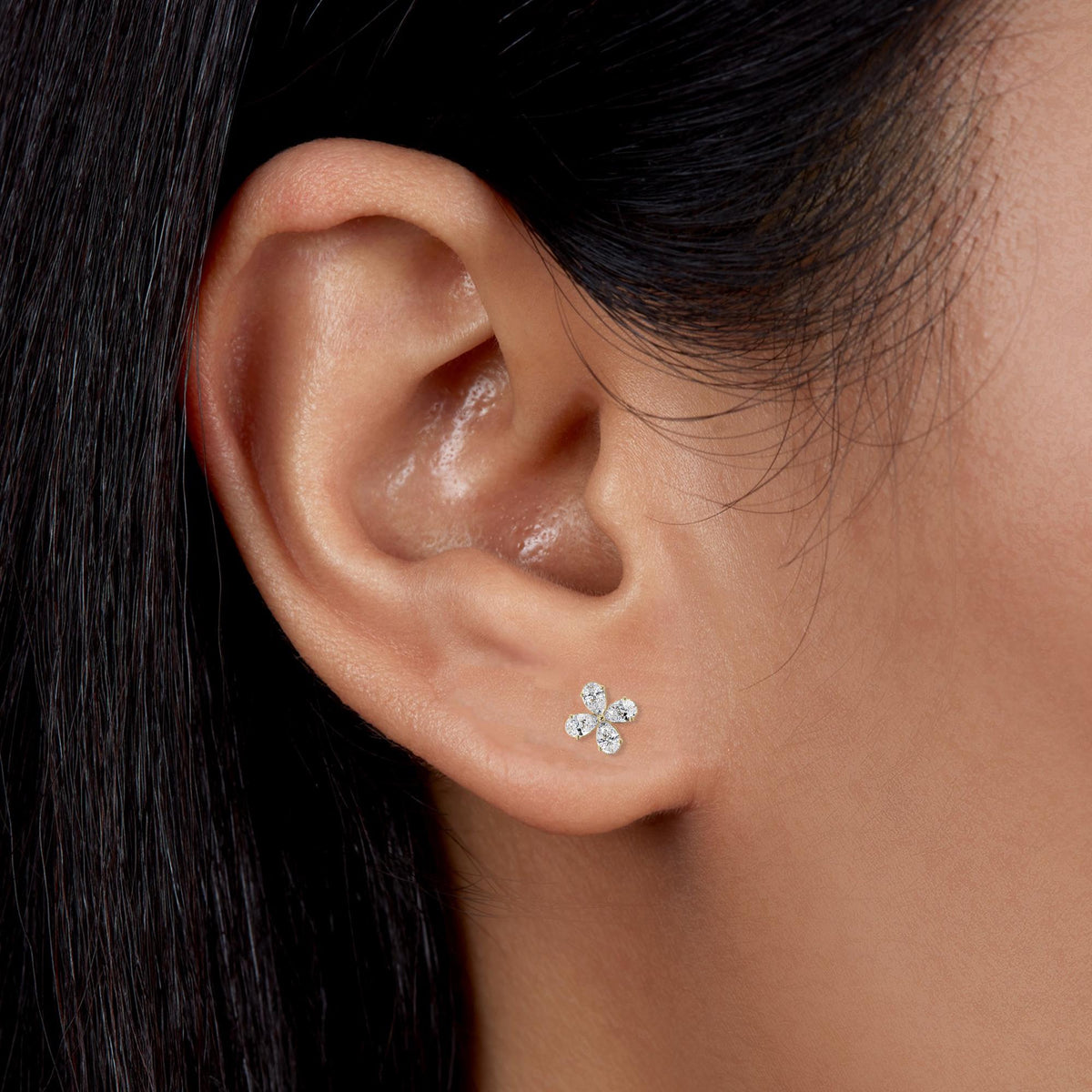 4K gold dainty diamond flower stud earring on the earlobe. The stud features four lab-grown pear-shaped diamonds arranged in a floral cluster, offering a minimalist and elegant everyday look.