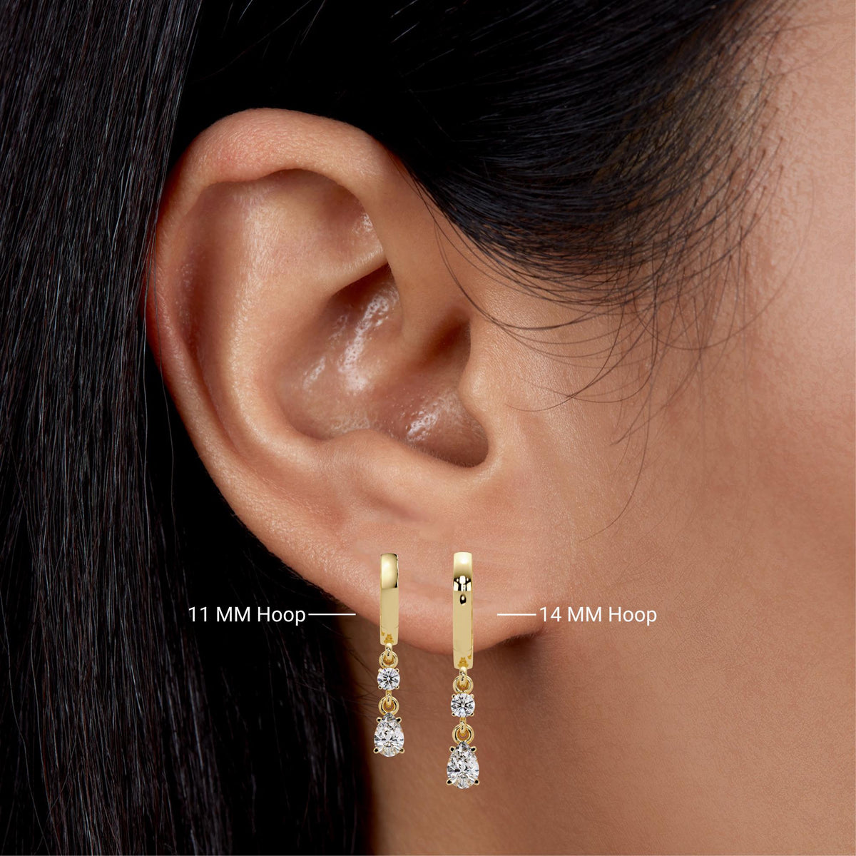 11mm and 14mm 14K yellow gold huggie earrings worn on a ear. Each earring features a lab-grown round diamond above a pear-shaped diamond, shown to compare hoop drop lengths for everyday wear.