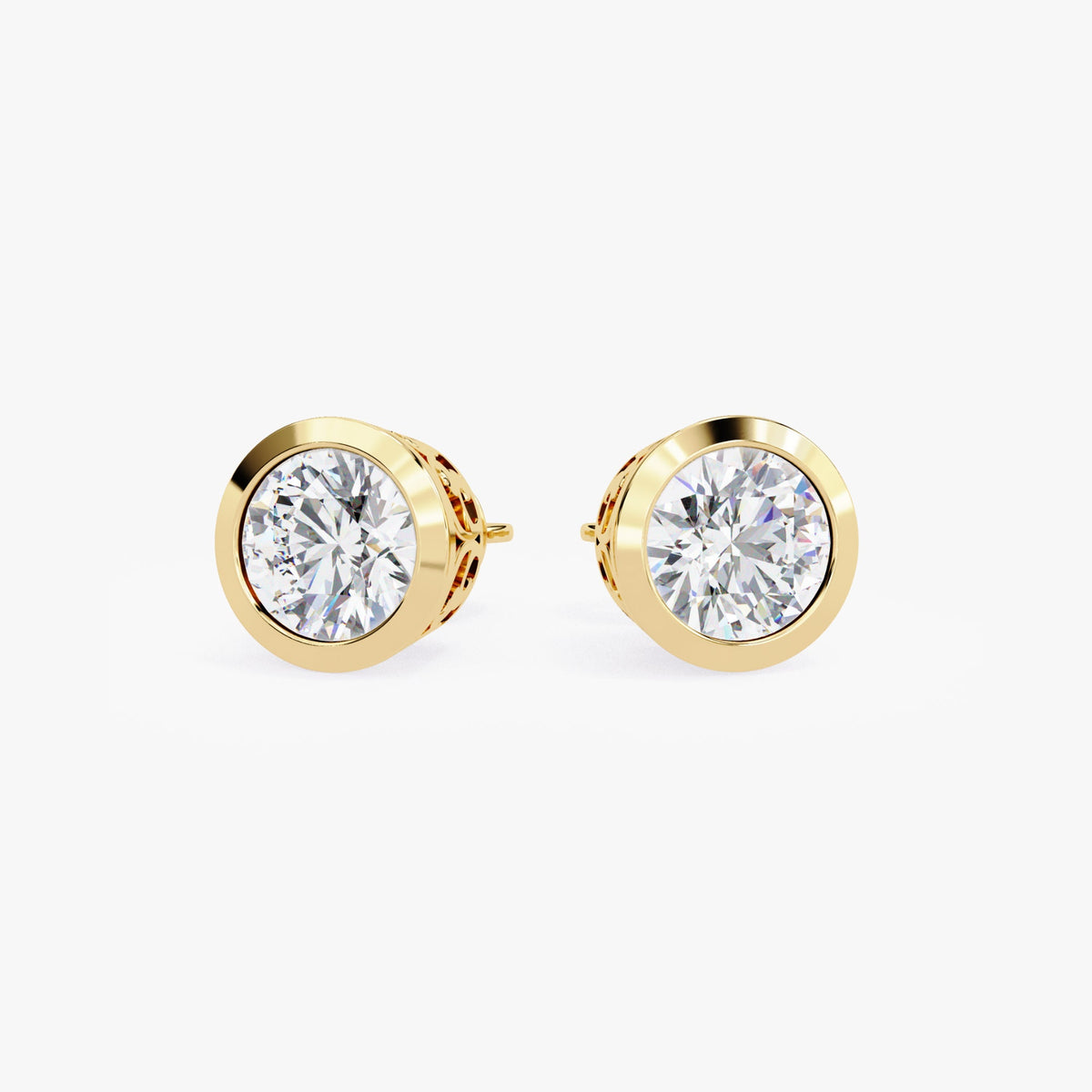May include: A pair of gold stud earrings with round, clear gemstones set in a bezel setting. The earrings have a delicate, intricate design around the gemstones.