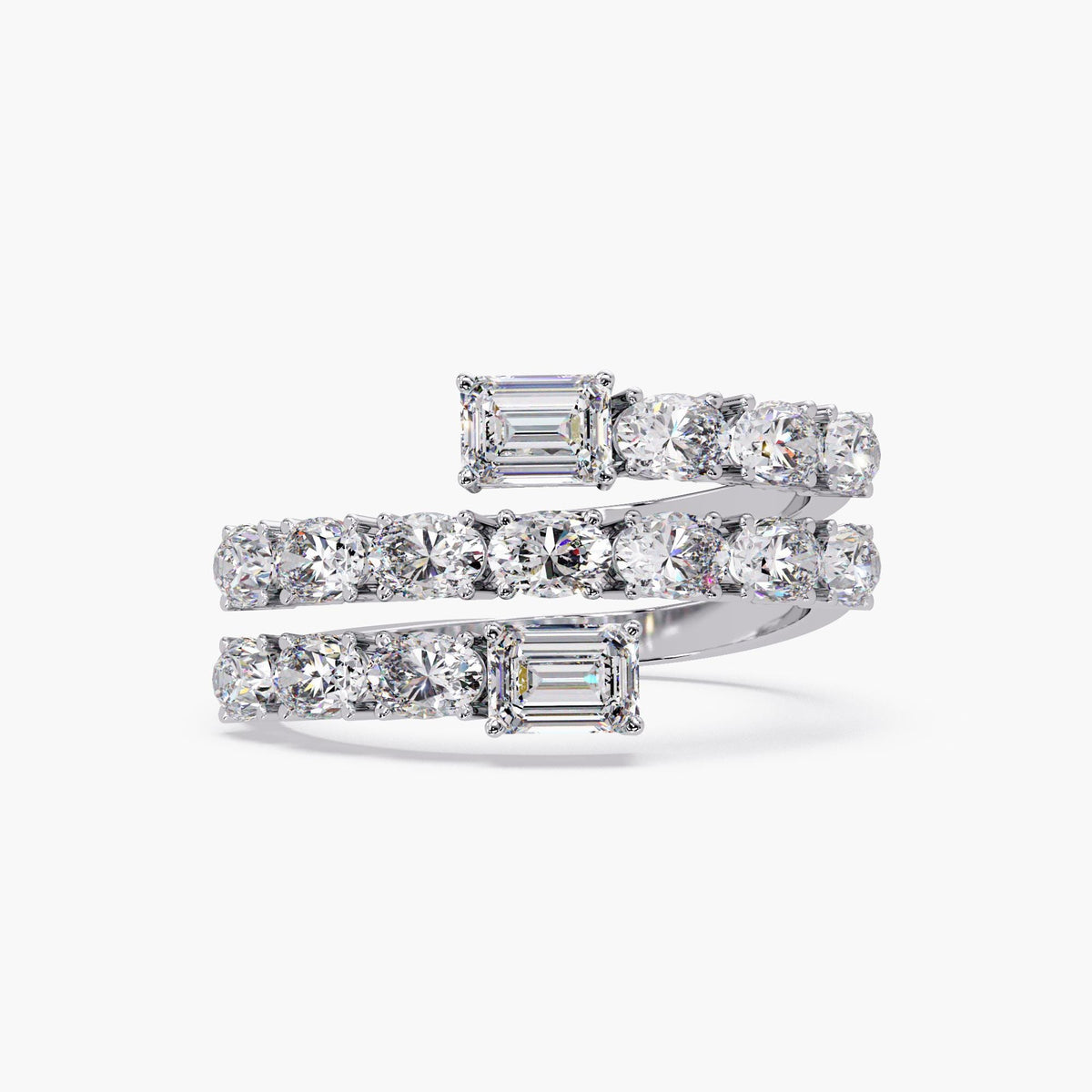 A close-up view of a three-row spiral wrap ring in white gold, showcasing two emerald cut diamonds at each open end. The band is set with multiple oval diamonds in a half eternity style, creating a layered bypass silhouette that curves fluidly around the finger.