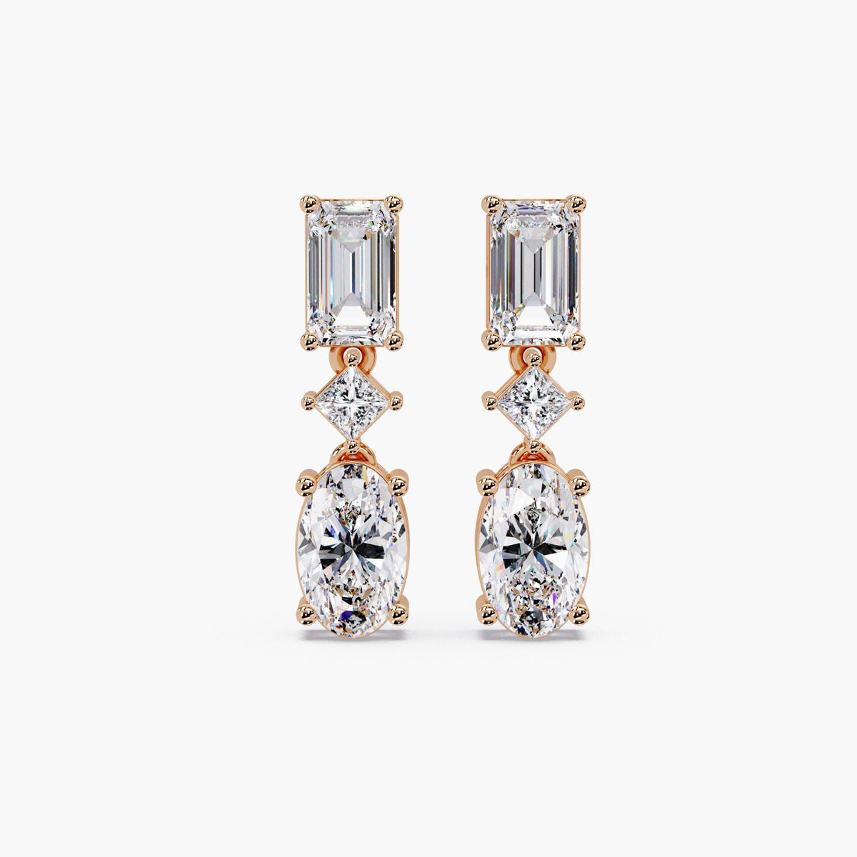Oval and emerald cut lab grown diamond drop earrings in 14K gold, featuring a graduated three stone design with oval diamonds and emerald accents.