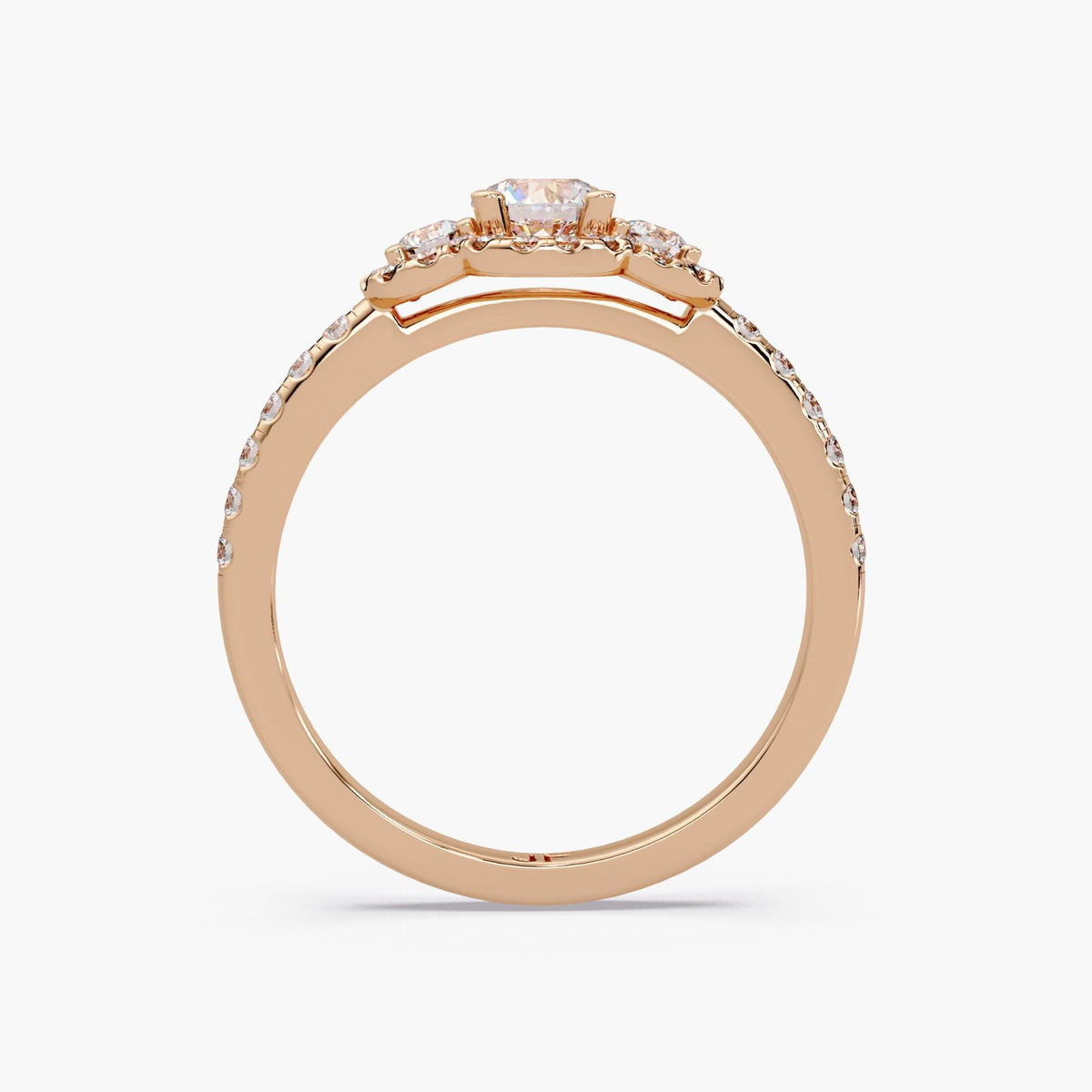 Round diamond halo trilogy engagement ring in 14K rose gold featuring three lab grown diamonds and pavé band with vintage style design.