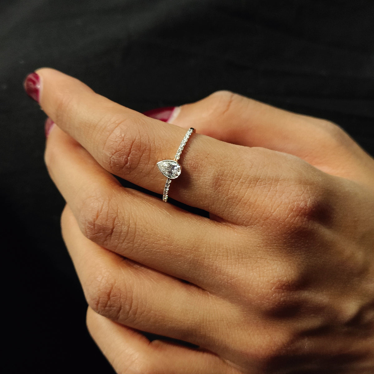 A pear-shaped diamond ring with a fine diamond-set band, worn on a hand.