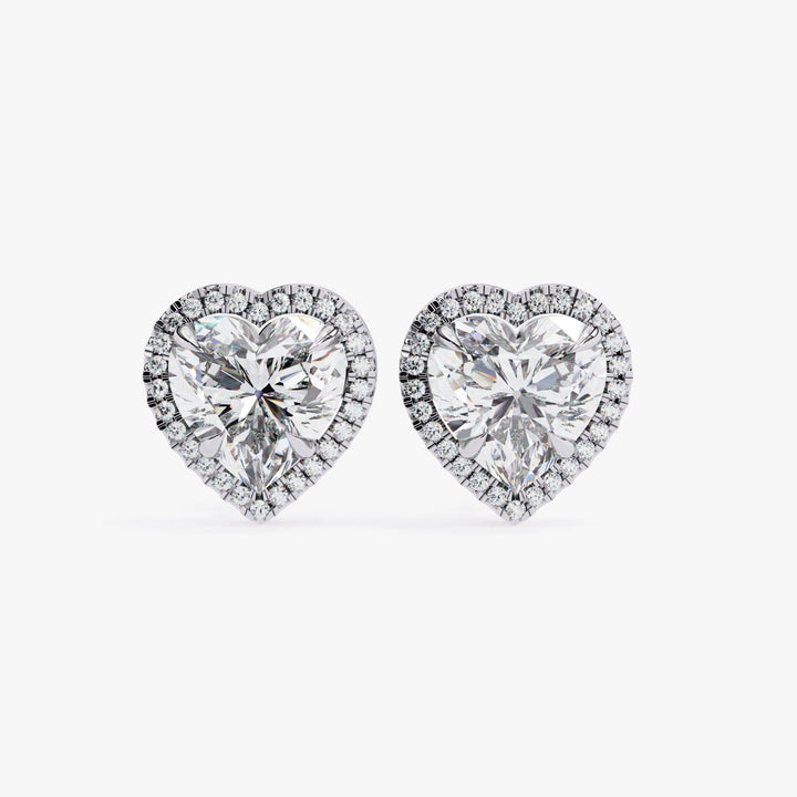 May include: Two heart-shaped diamond earrings with a halo of smaller diamonds around the center stone. The earrings are silver in color.