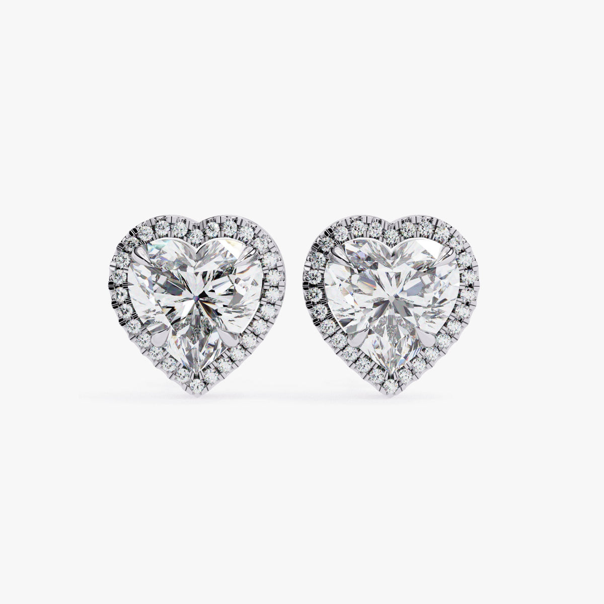 May include: Two heart-shaped diamond earrings with a halo of smaller diamonds around the center stone. The earrings are silver in color.