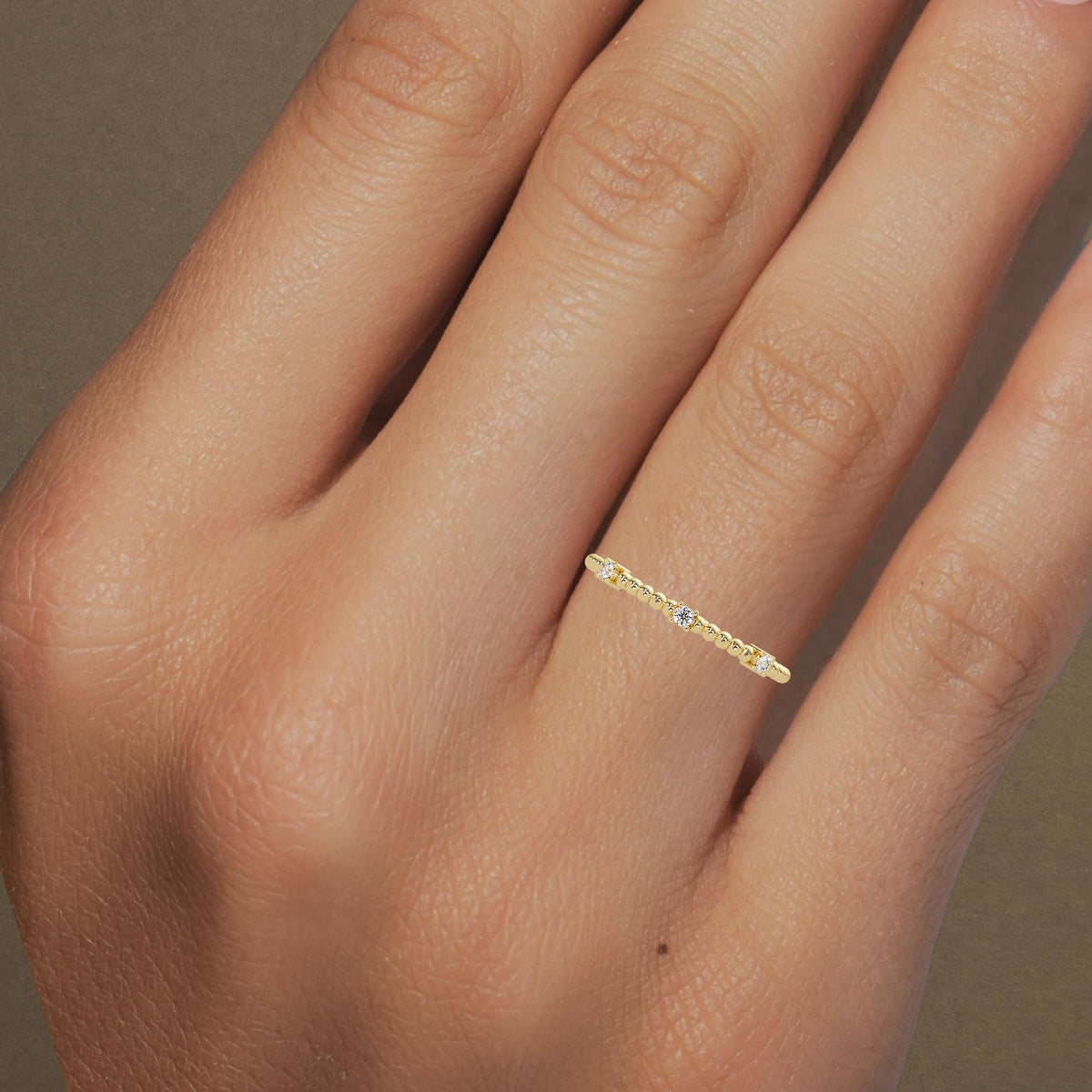 Close-up of a hand wearing a thin 14K yellow gold ring featuring three small round diamonds spaced evenly along a delicate beaded band.