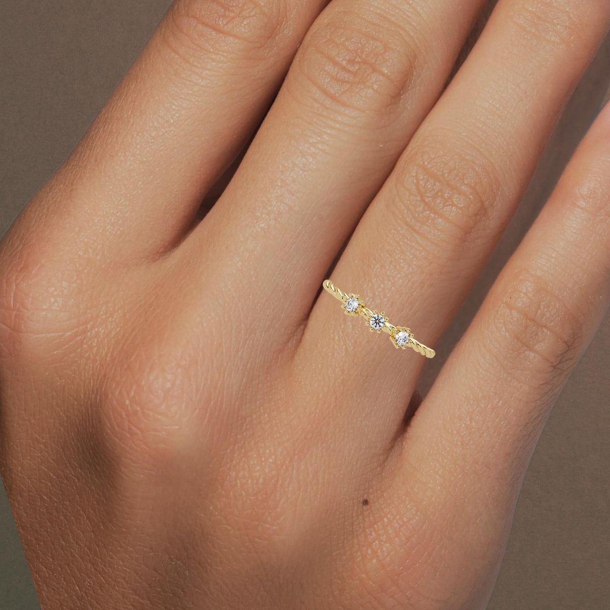 Hand wearing a 14k yellow gold twisted band ring with three small round natural diamonds in floral prong settings, showing the ring’s delicate and stackable fit.