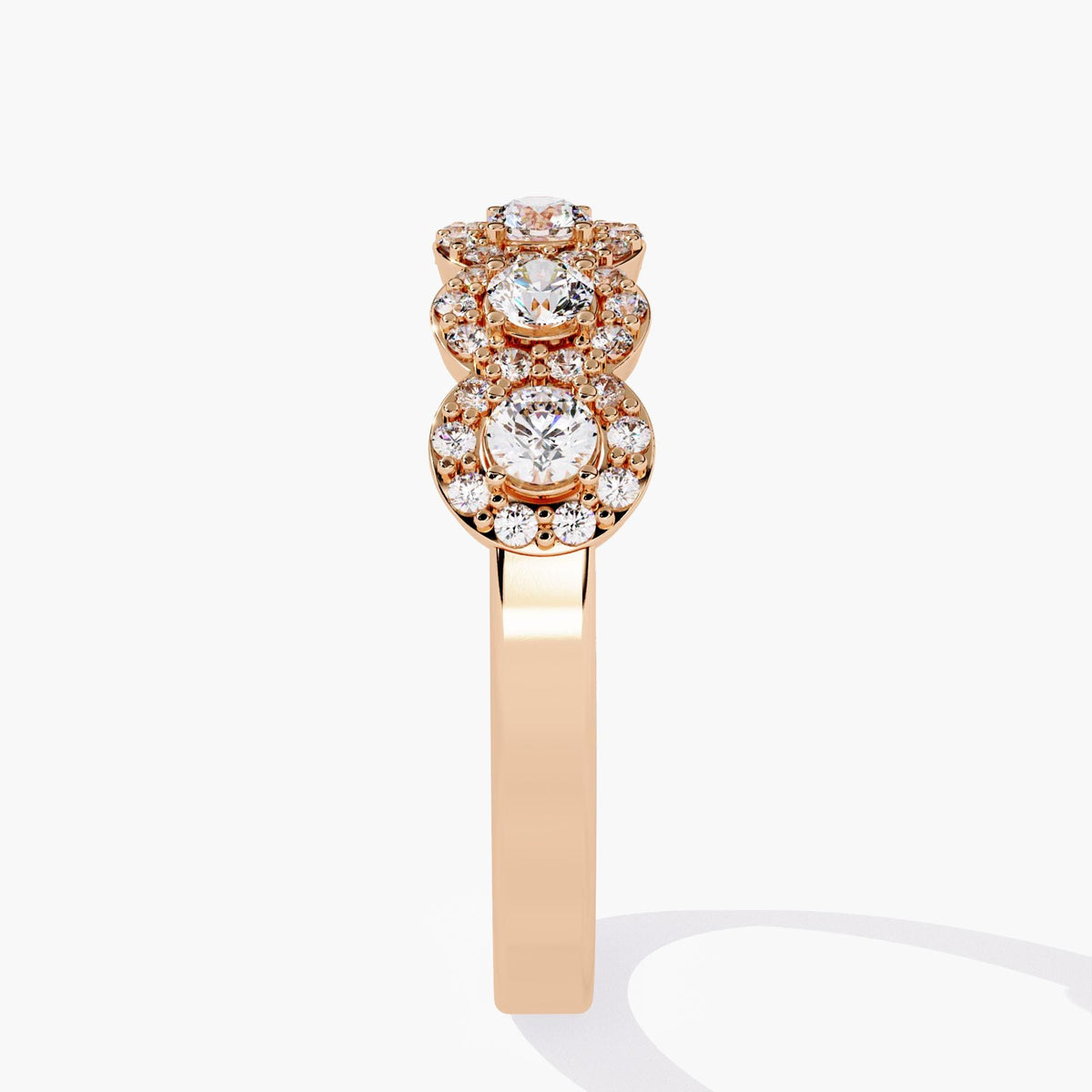 Side profile of a 14k rose gold ring showing the stacked height of three raised halo diamond clusters. The polished band and layered setting add dimension, giving the ring a bold, sculptural presence suited for statement bridal or anniversary wear.