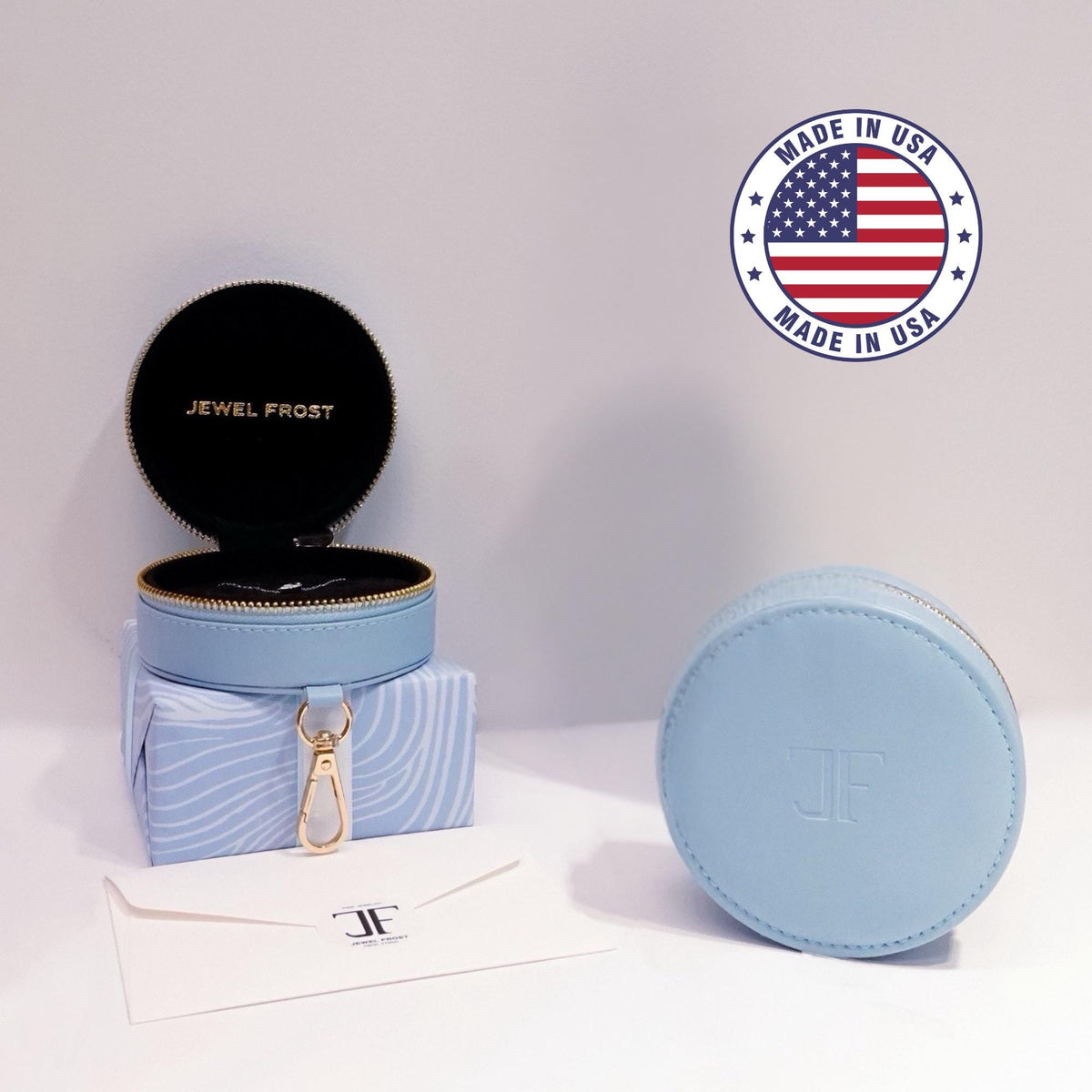 Jewel Frost signature packaging including a blue round zippered gift box, branded envelope, and Made in USA badge. The open box reveals a velvet interior with gold zipper detail and clip.