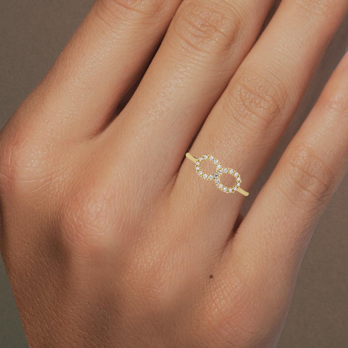 Hand wearing a 14k yellow gold infinity diamond ring with pavé-set lab grown diamonds, showing its delicate size and stackable fit.