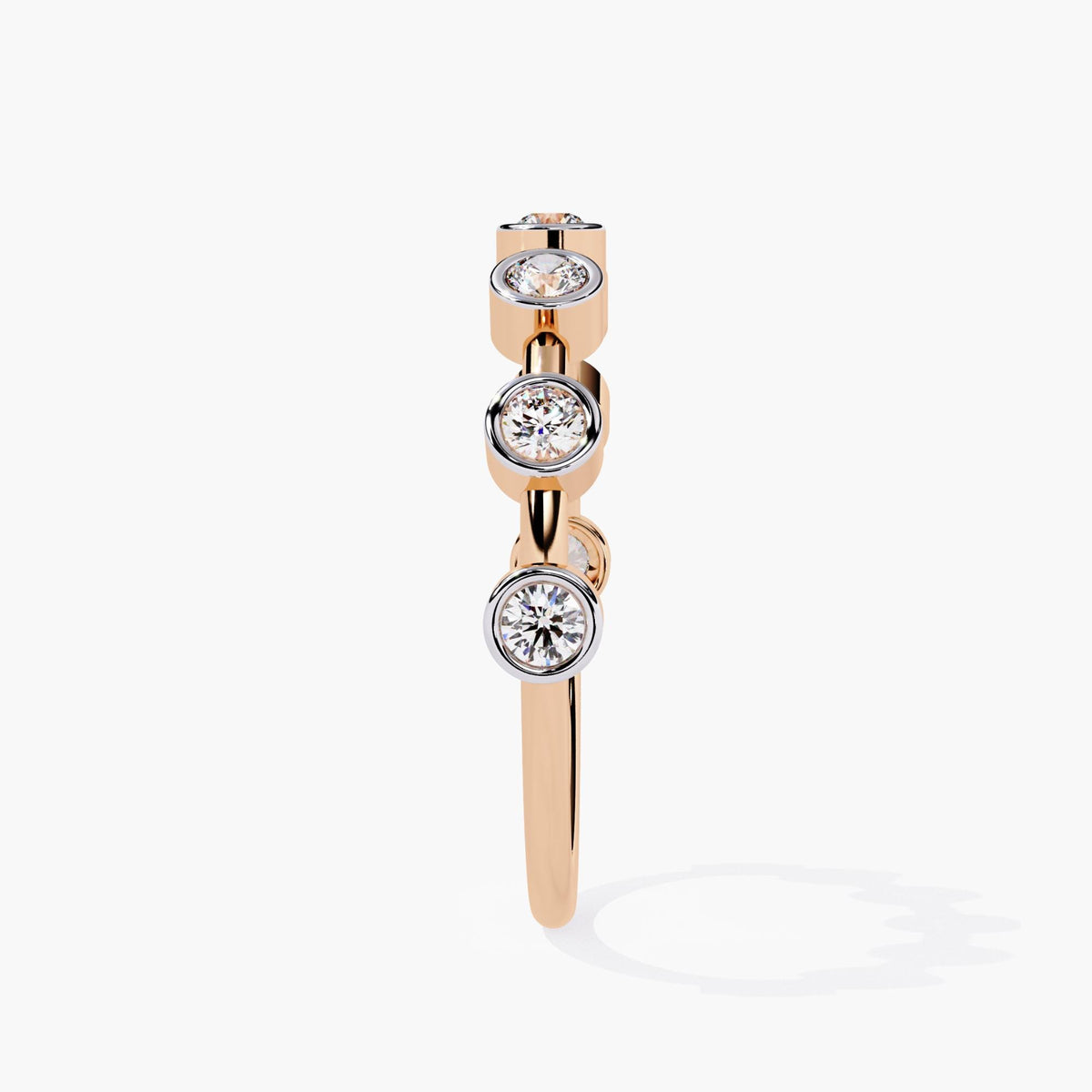 A side view of a rose gold stacking ring featuring round diamonds set in polished bezel settings.  The white gold bezels contrast with the warm rose gold band, highlighting the sparkle of the diamonds. This design offers a minimalist, aesthetic, perfect for stacking or wearing as a standalone piece.