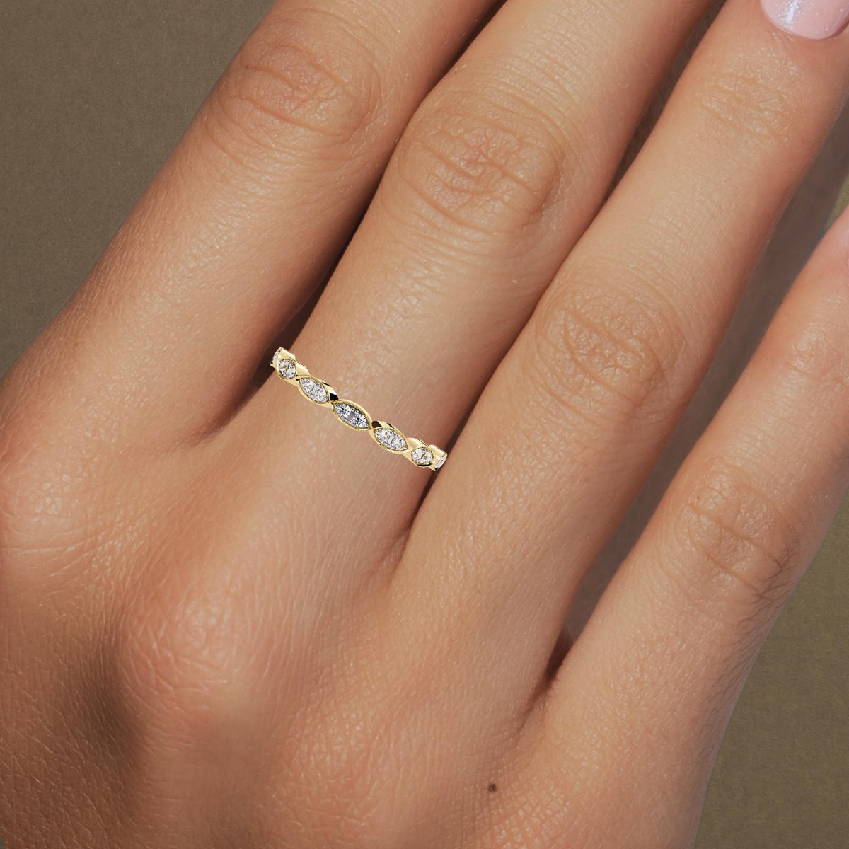 A close-up of a yellow gold ring worn on a finger, featuring marquise-shaped settings with round diamonds. The diamonds are set in a bezel design, creating a sleek and modern look. The alternating diamond pattern adds a sophisticated touch to the simple band, making it ideal for stacking or wearing alone as a minimalist statement piece.