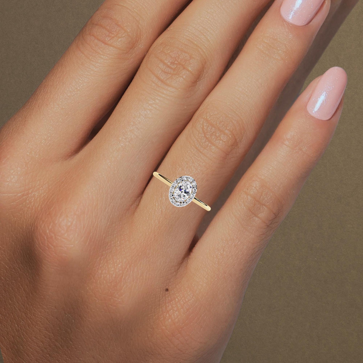A hand wearing a 14k yellow gold oval halo engagement ring. The ring features a 0.35 ct oval lab diamond at the center, surrounded by a halo of smaller round diamonds on a slim polished gold band. The style appears elegant and minimal, perfect for proposals or bridal wear.
