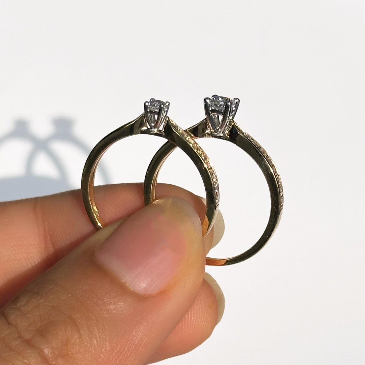 Side view of two 18K gold solitaire rings with round lab-grown diamonds in four-prong settings, tapered shanks and half eternity pavé band detailing.