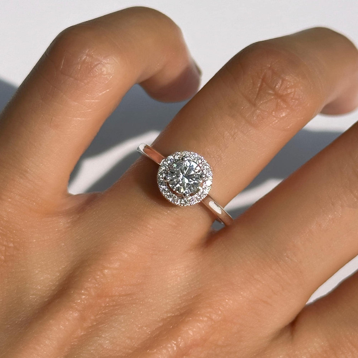 18K Gold Halo Diamond Ring featuring a round brilliant lab-grown diamond center stone (0.50ct), surrounded by pavé diamonds in a halo setting. Dainty, minimalist design worn on hand in natural light. Promise, engagement ring or birthday gift for her.