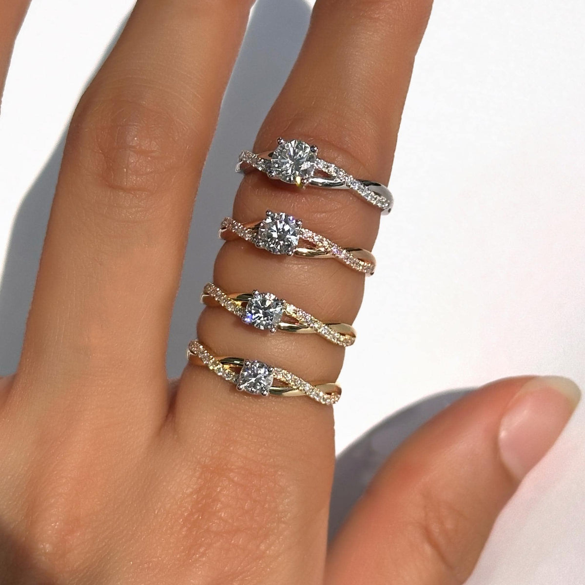 Close-up of a hand wearing 18K gold twisted engagement rings in white, rose, and yellow gold. Each ring features a round lab-grown diamond set on a pavé band with a twist shank.