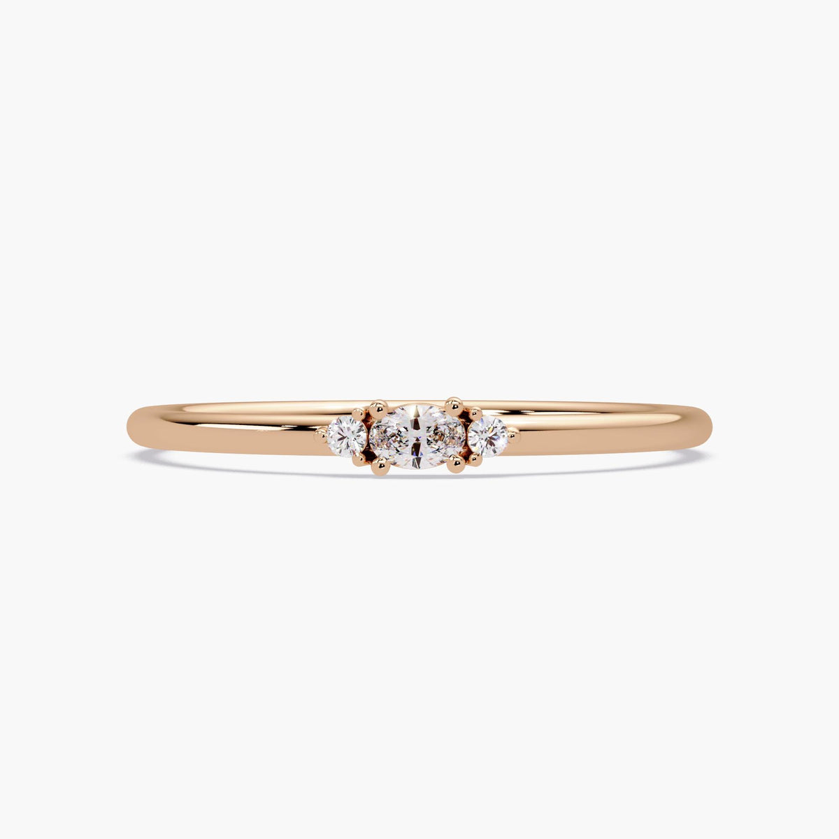 14K rose gold ring with a center oval-cut lab-grown diamond and two round diamonds set in a three-stone design on a slim band.