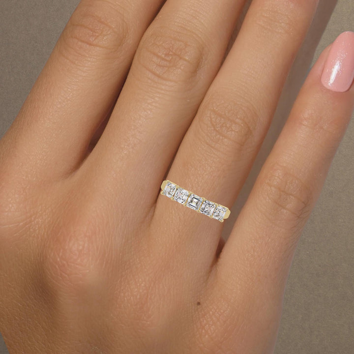 Five-stone Asscher cut lab-grown diamond band in 14K yellow gold shown on hand, perfect as a modern wedding or anniversary ring.