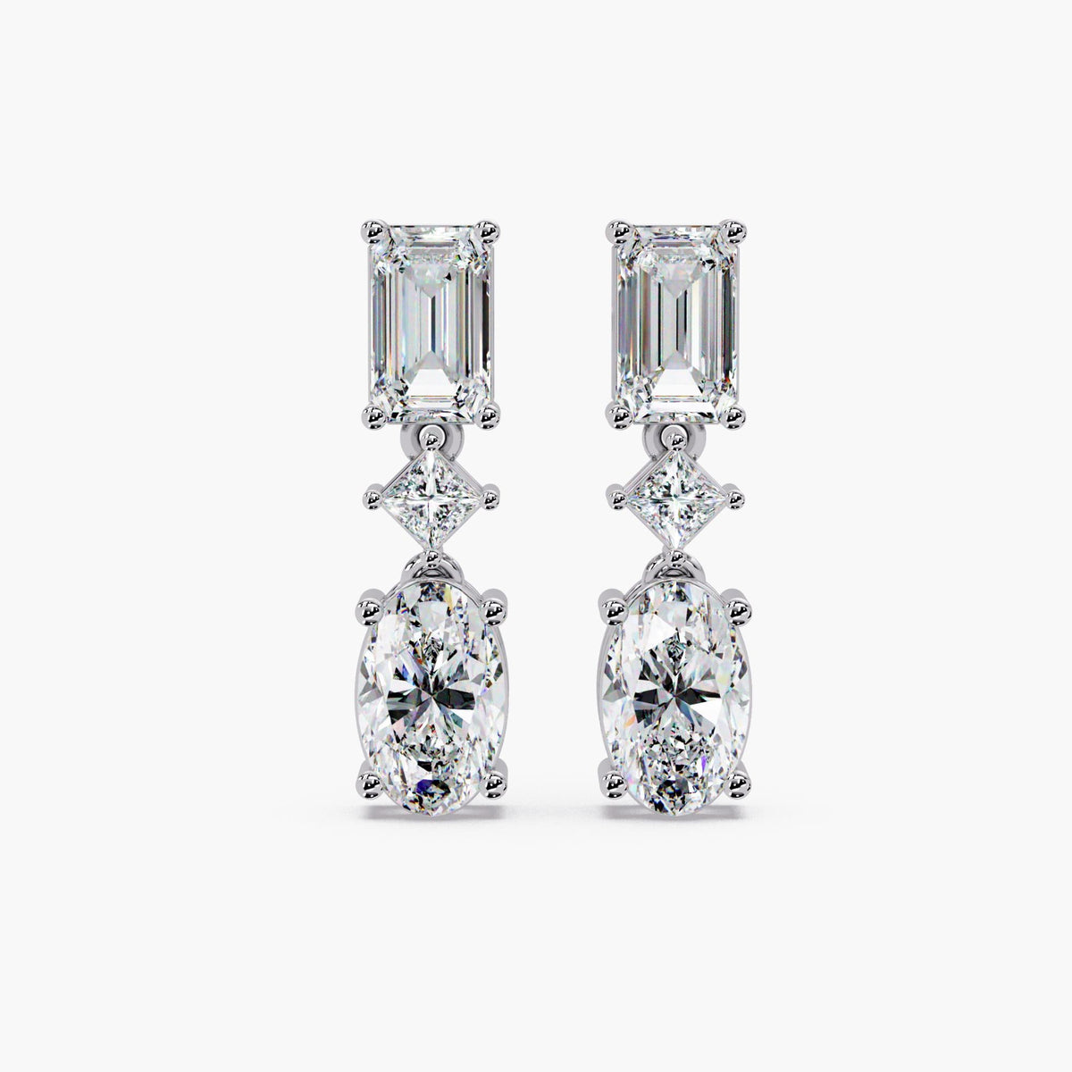 Oval and emerald cut lab grown diamond drop earrings in 14K gold, featuring a graduated three stone design with oval diamonds and emerald accents.