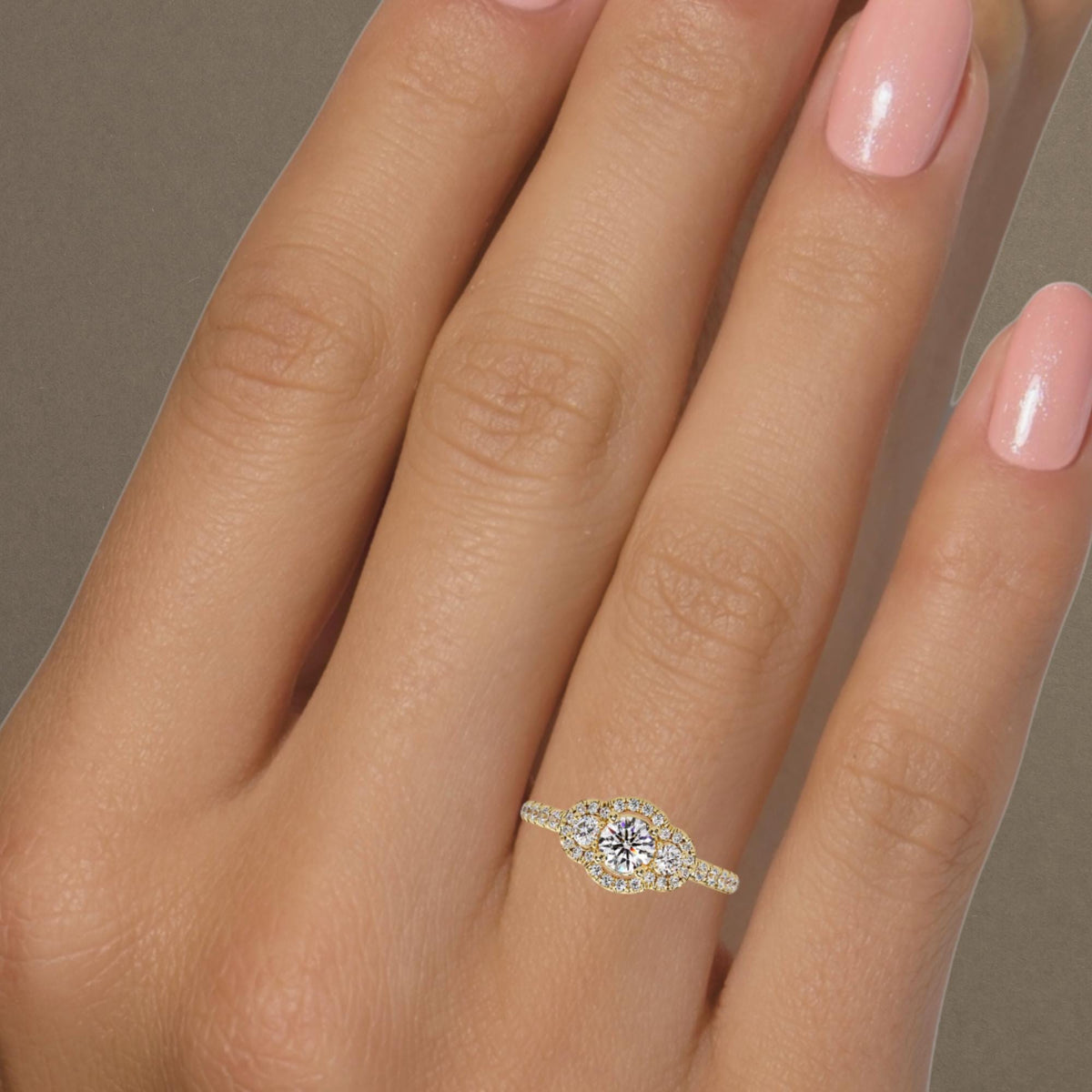 Round halo trilogy engagement ring with lab grown diamonds worn on hand, delicate 14K gold band with three stone diamond cluster design.