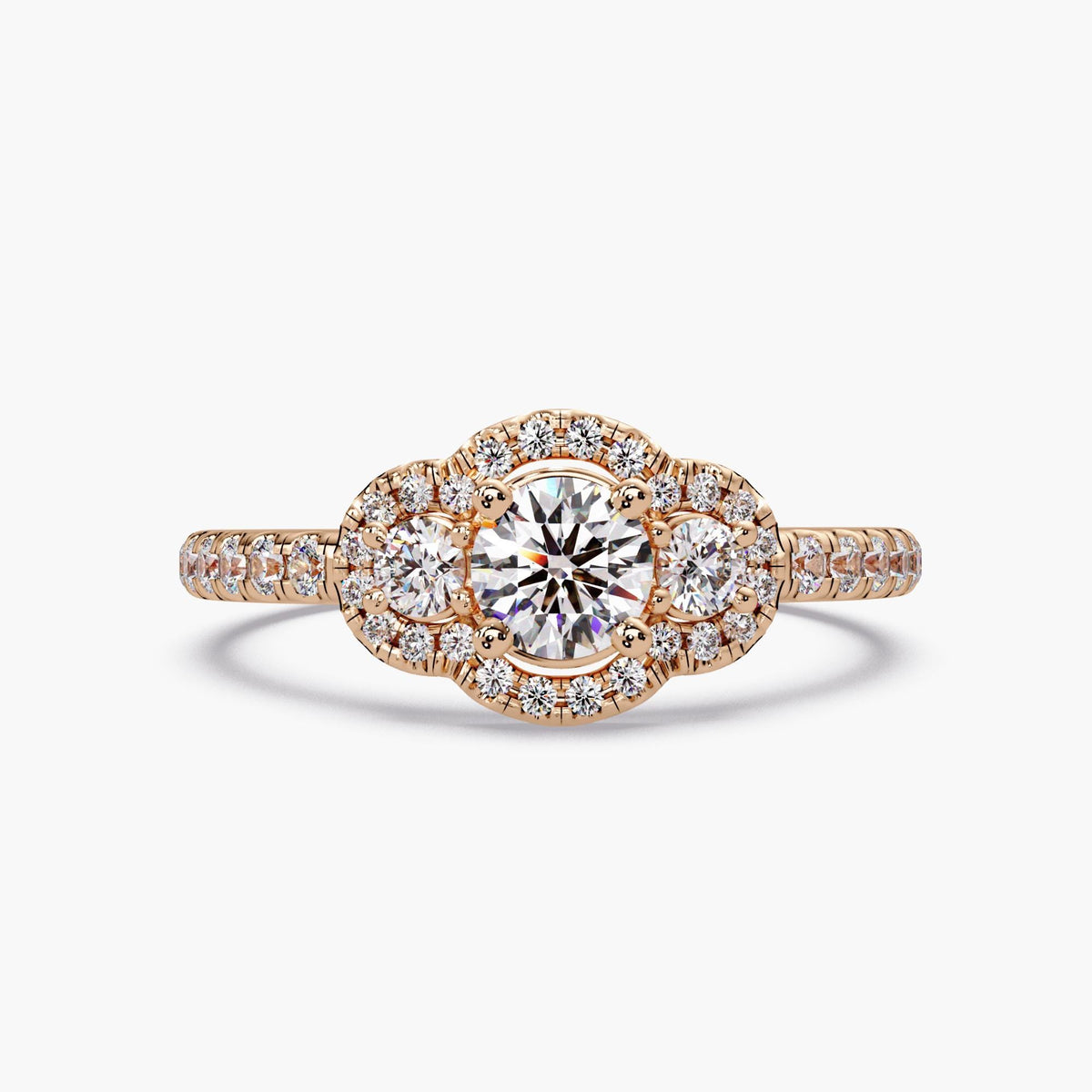 Round diamond halo trilogy engagement ring in 14K rose gold featuring three lab grown diamonds and pavé band with vintage style design.