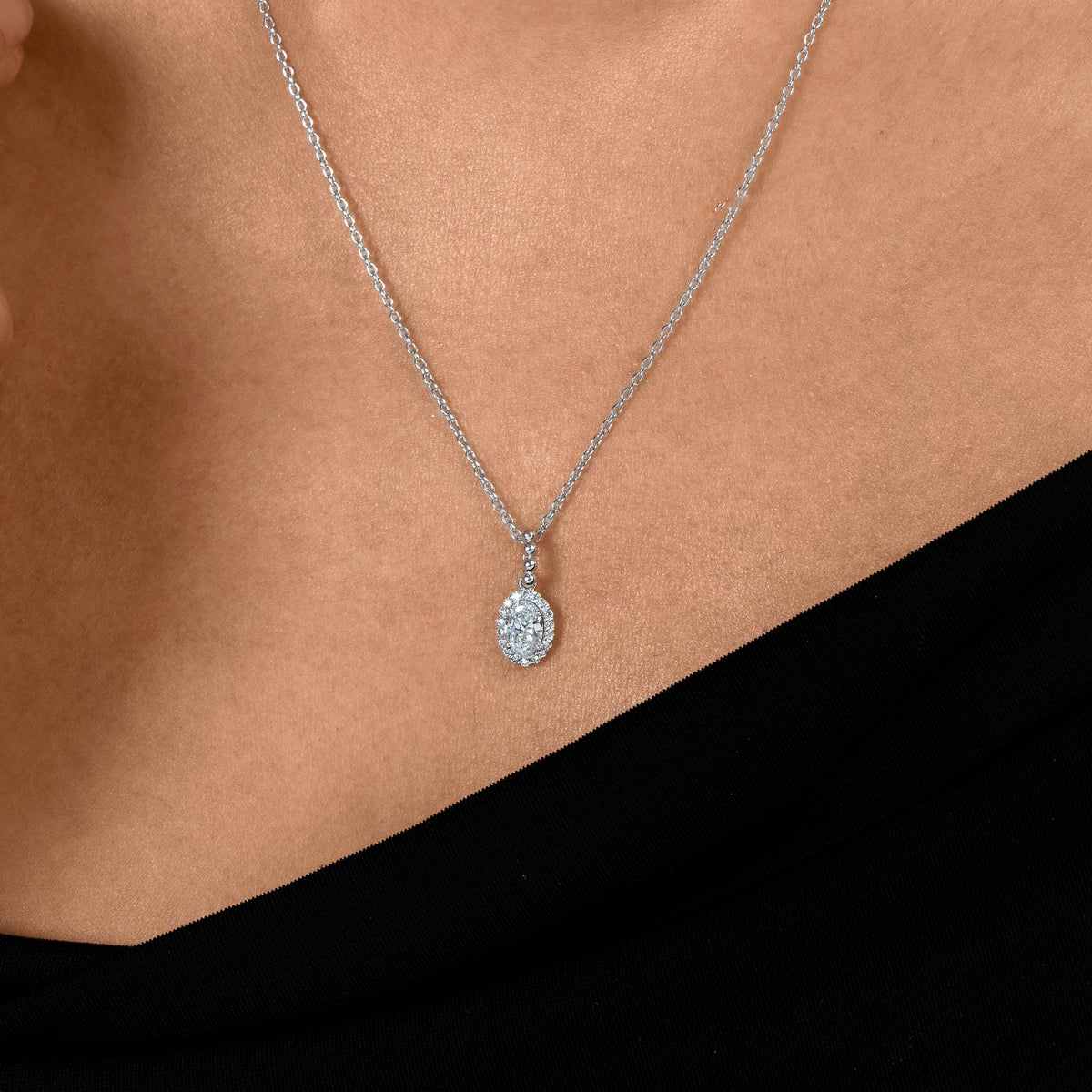 14K gold oval halo natural diamond pendant necklace with 0.50 CTW diamonds on a dainty chain, worn at the neckline.