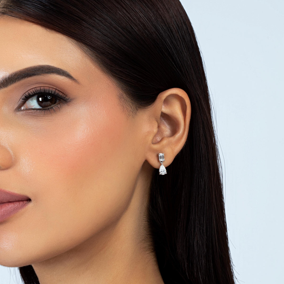 14K white gold lab-grown diamond drop earring with an emerald-cut stud and pear-shaped diamond dangle, worn on an ear.